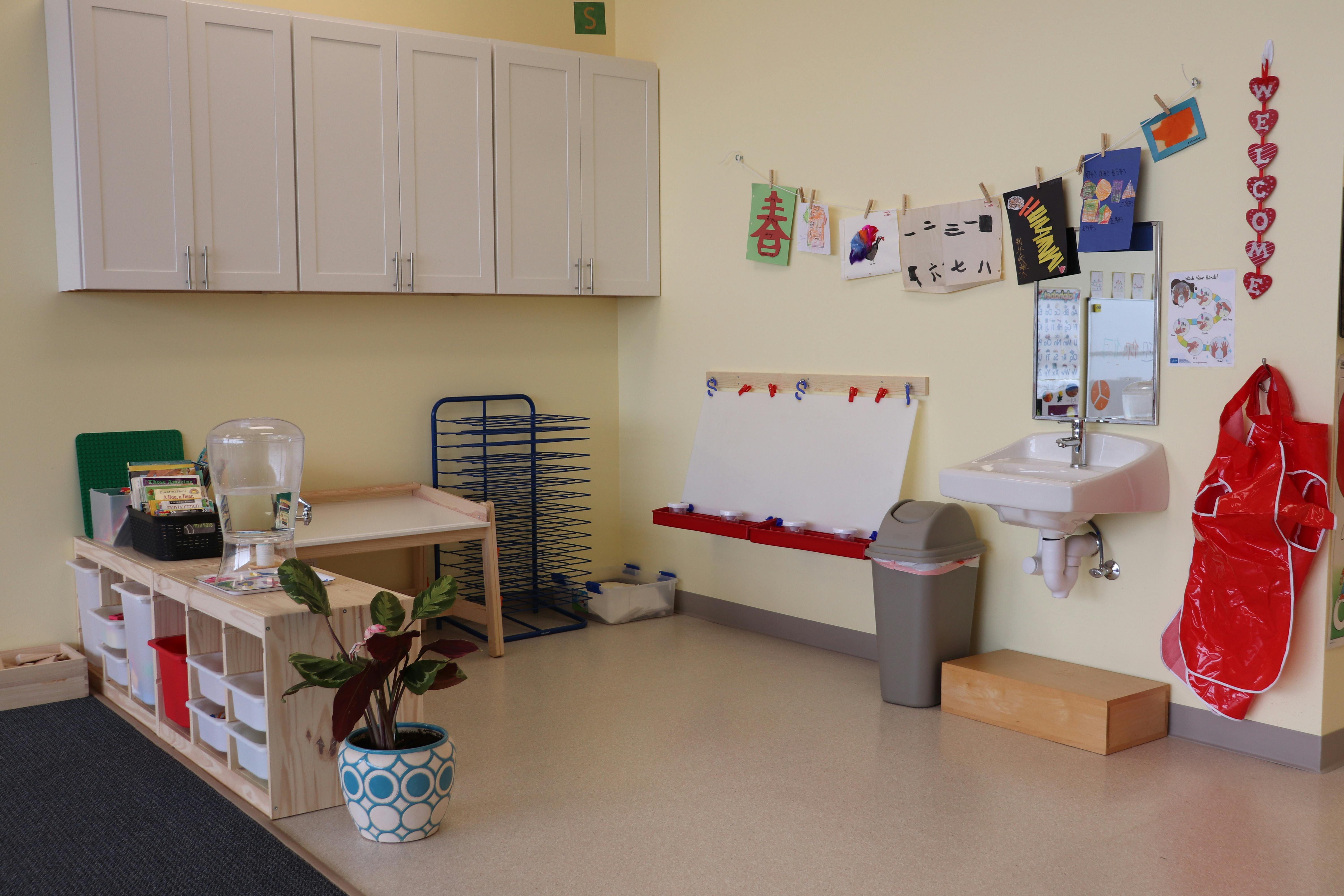 Classroom with white cabinets, sink, and children's artwork on wall