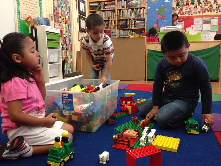 Three children playing with building blocks and toys on a blue mat