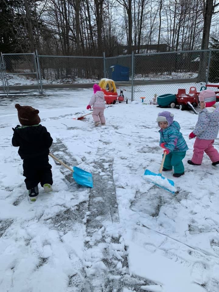 Children shoveling snow in a fenced area