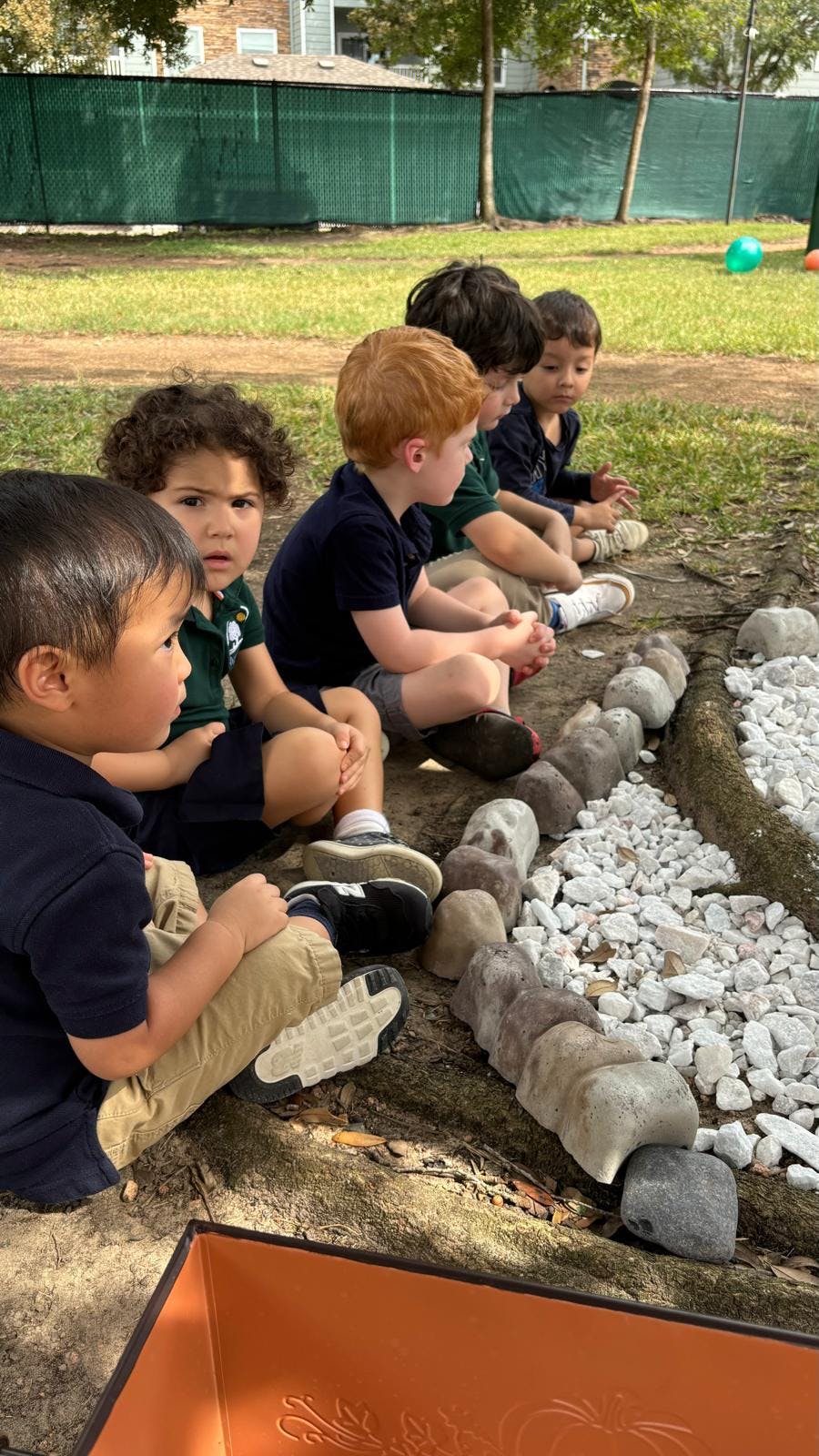 Children sitting on the ground next to a rock and gravel border