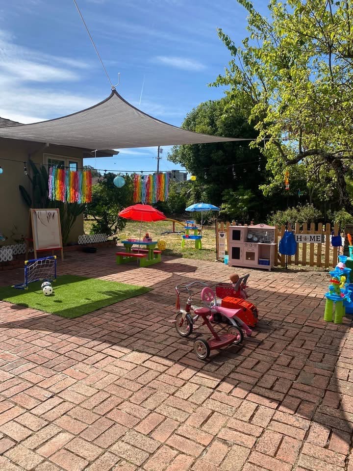Playground area for children with toys and a shade sail on a brick patio