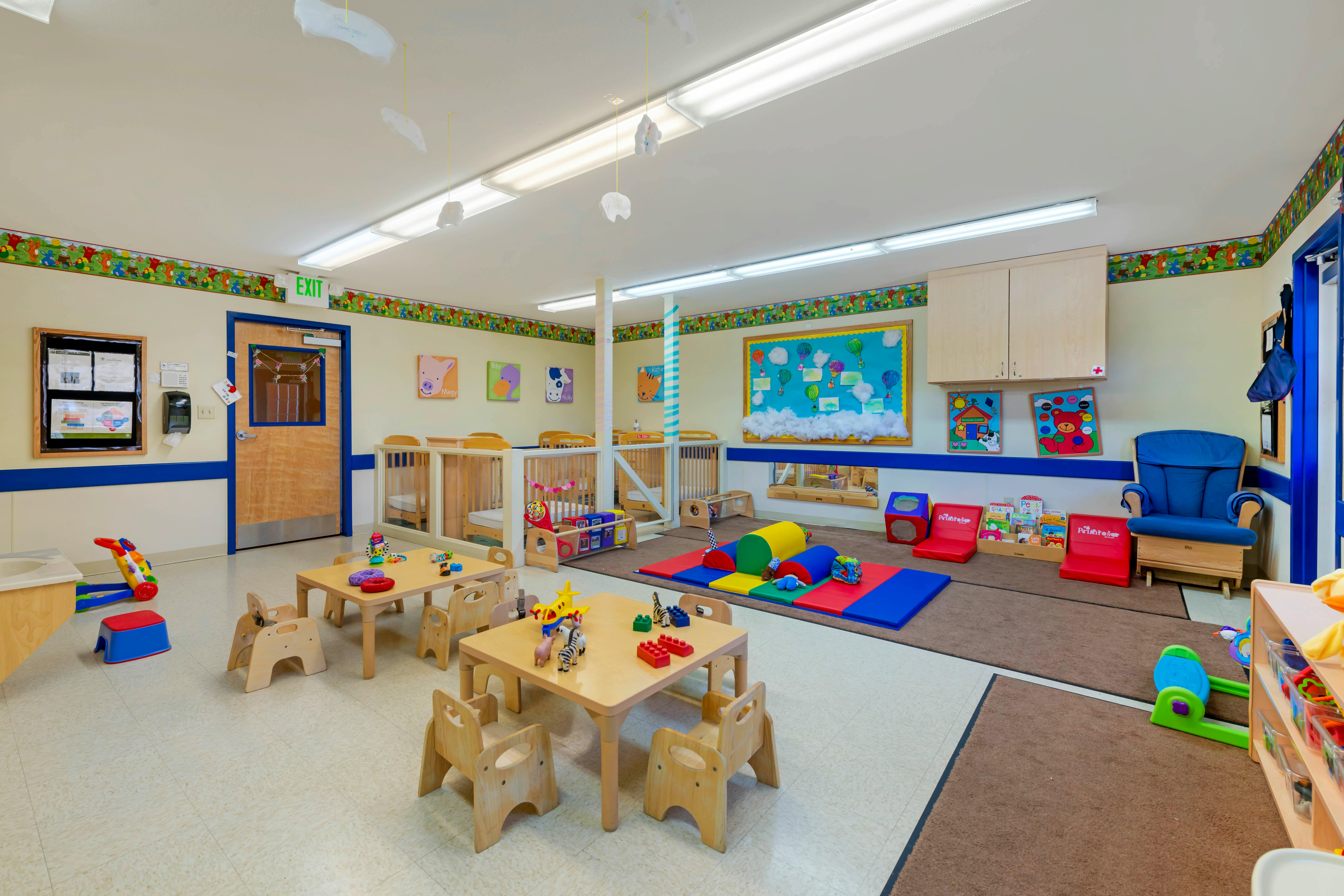 Colorful playroom with cribs, small tables, and play mats