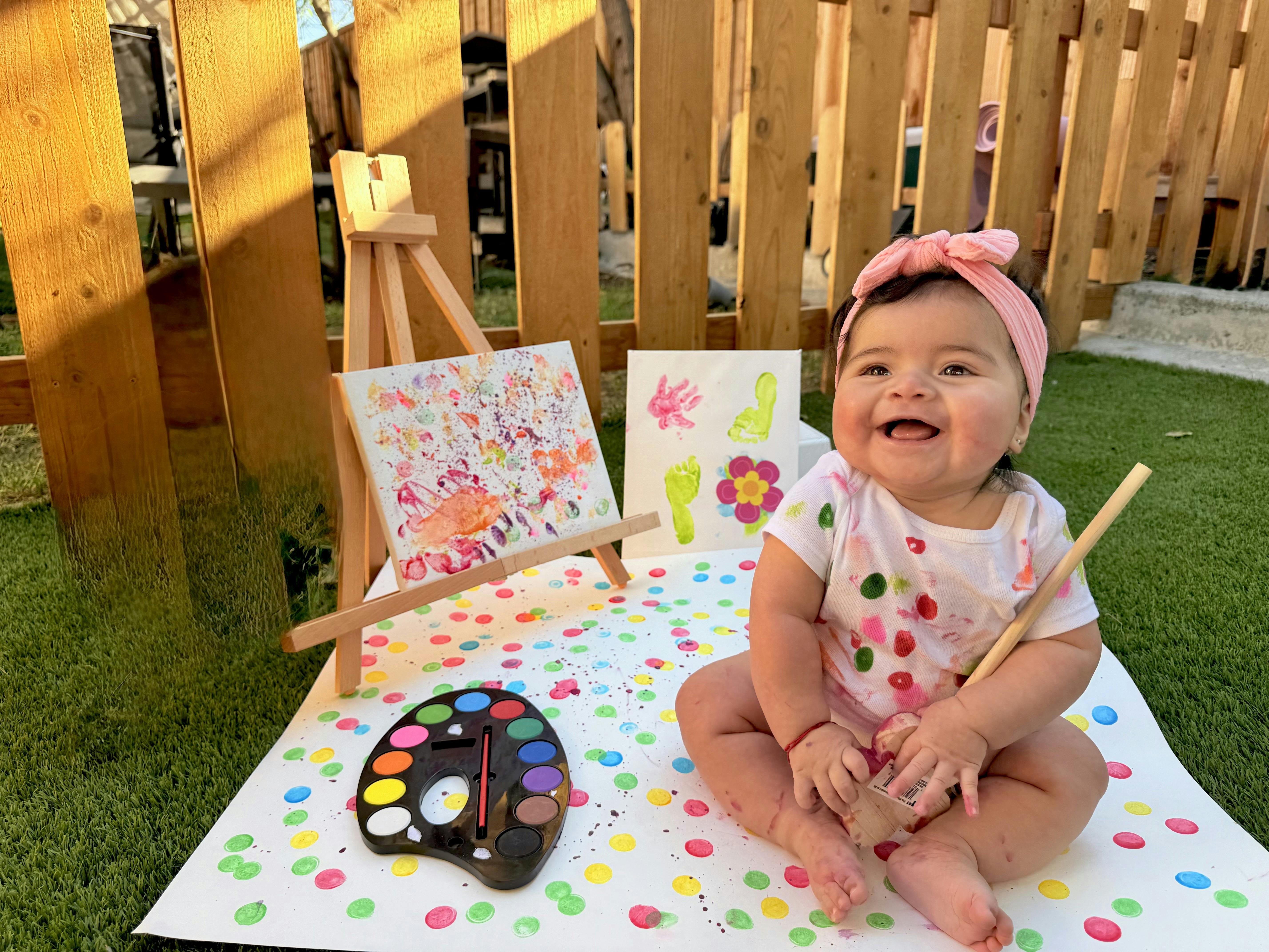 Child sitting on a polka dot mat with an easel, painting, and paint palette