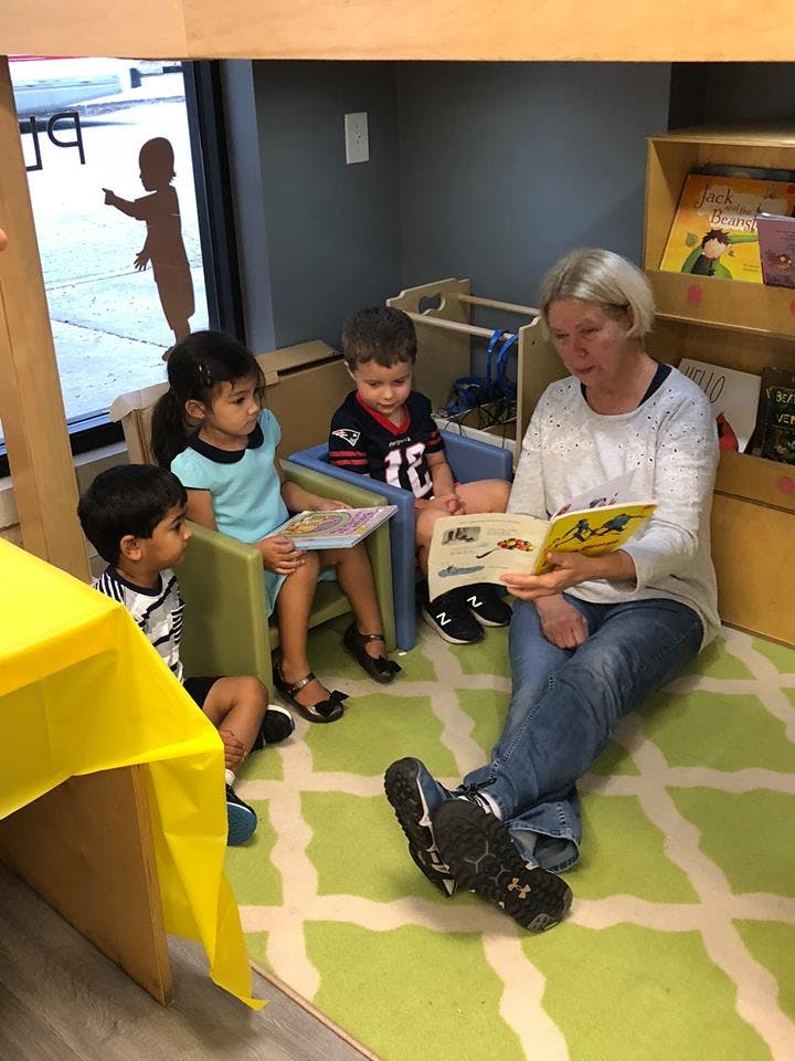 Adult reading a book to three children in a classroom