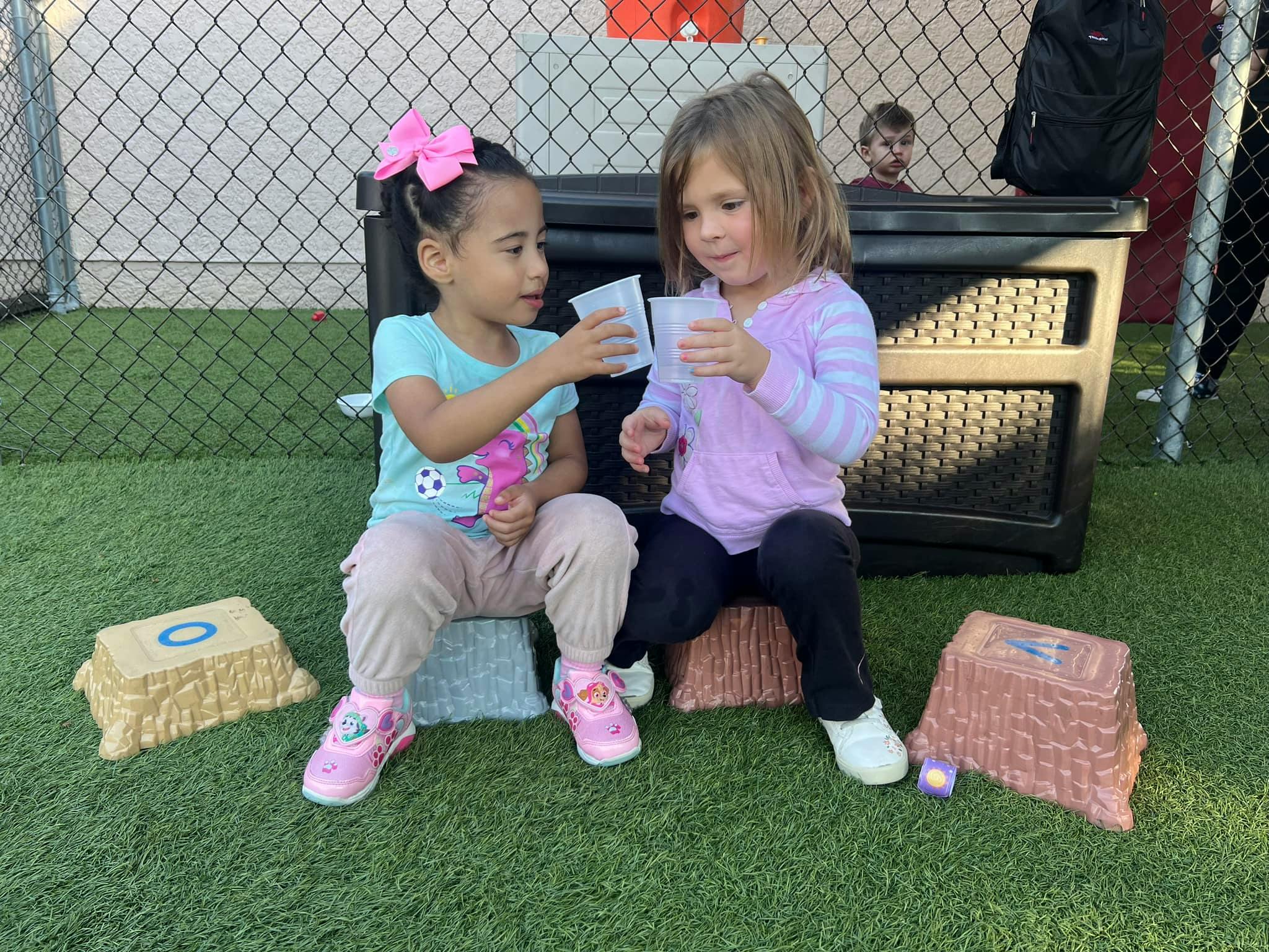 Two children sitting on artificial grass holding cups