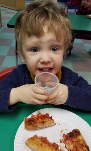 Child holding a cup with pizza slices on a plate