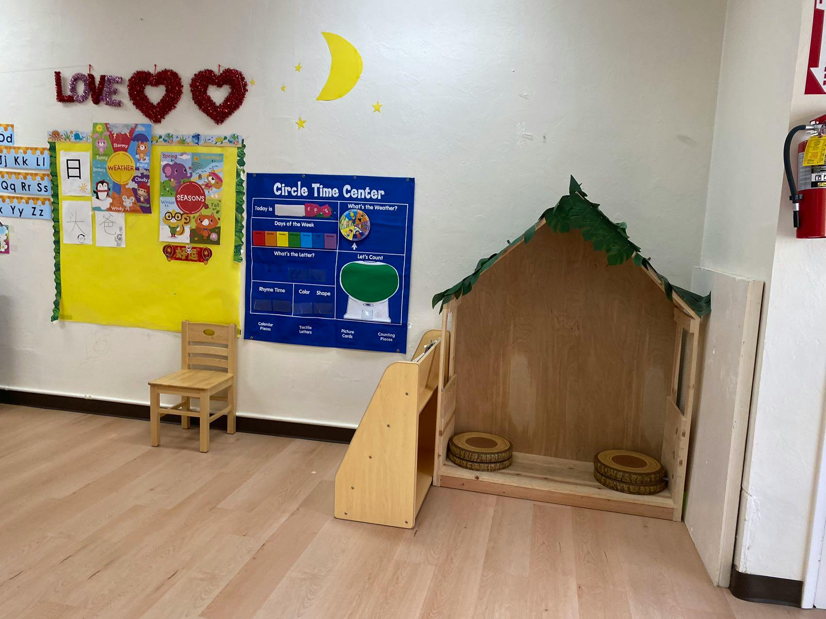 Classroom corner with a wooden playhouse, chair, and bulletin boards