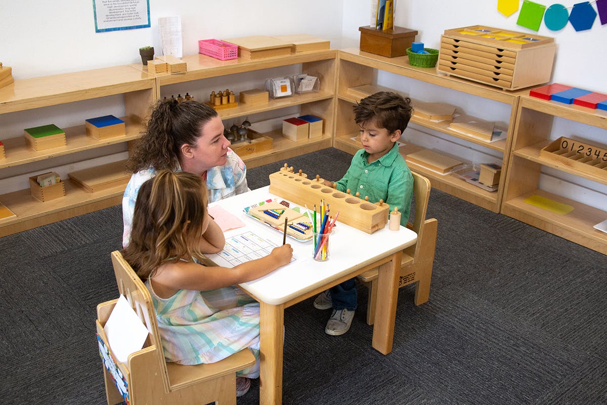 Adult and two children at a table with school supplies in a classroom
