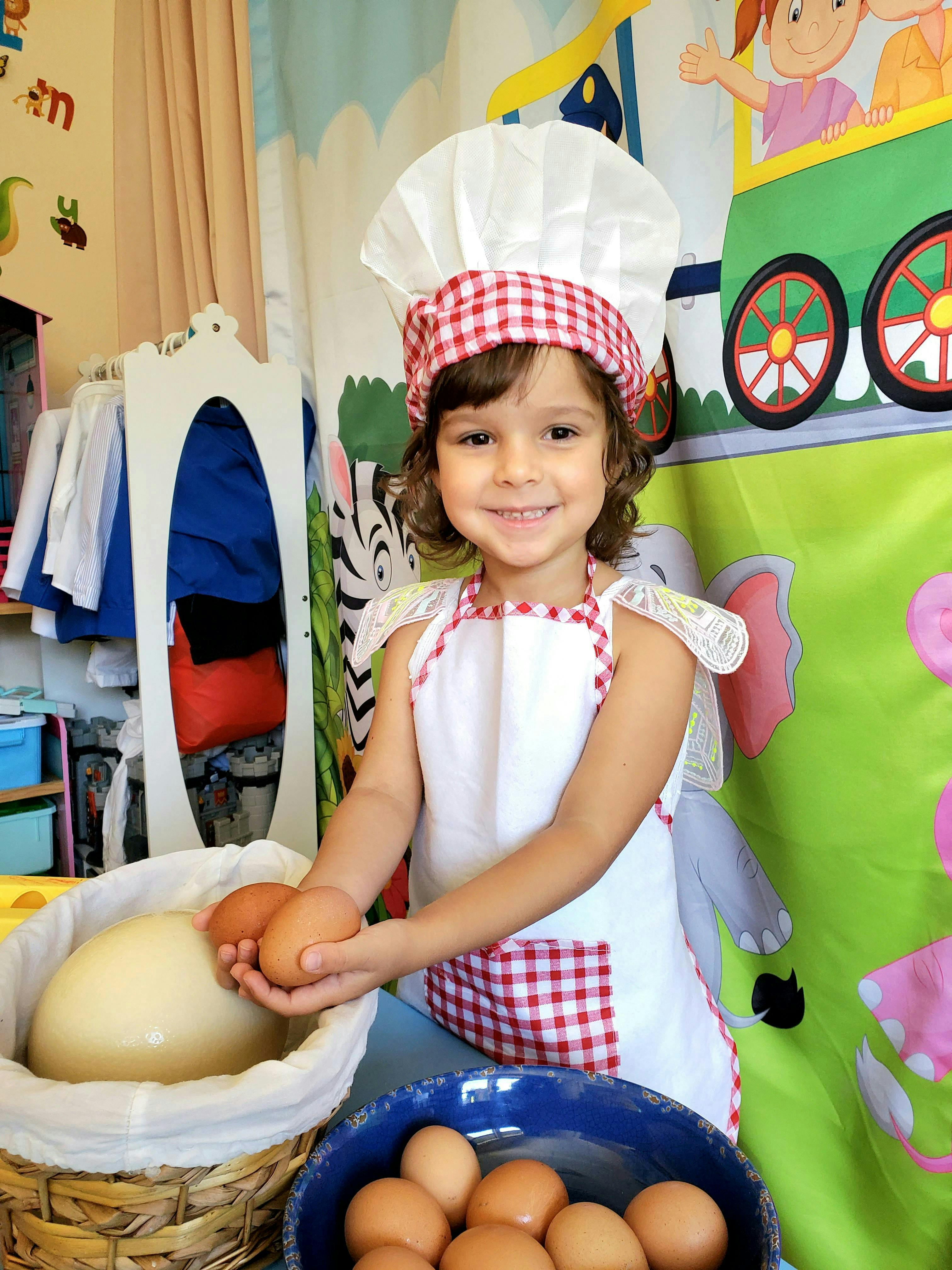 Child in a chef's hat and apron holding eggs