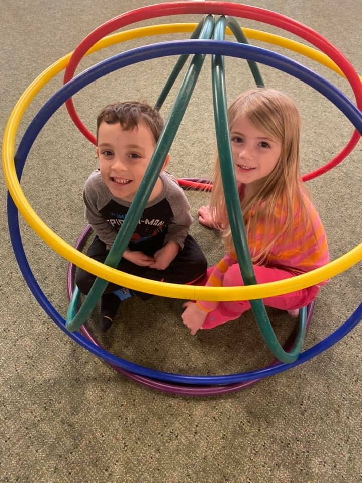 Two children sitting inside a structure made of colorful hoops