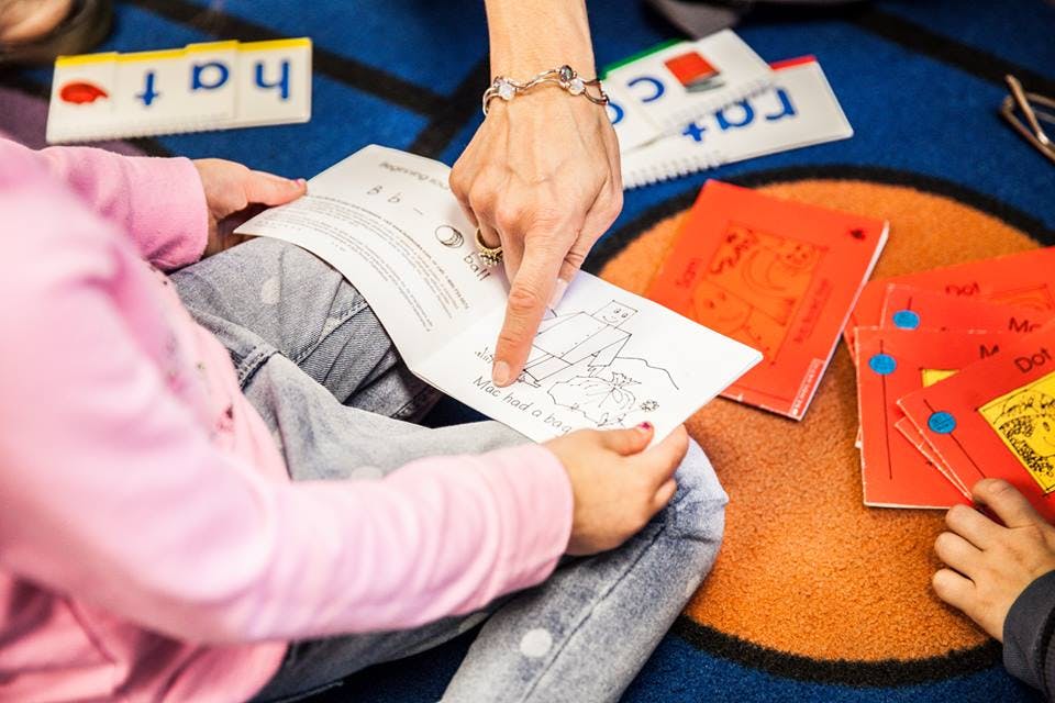 Adult hand pointing at a drawing in a book held by a child