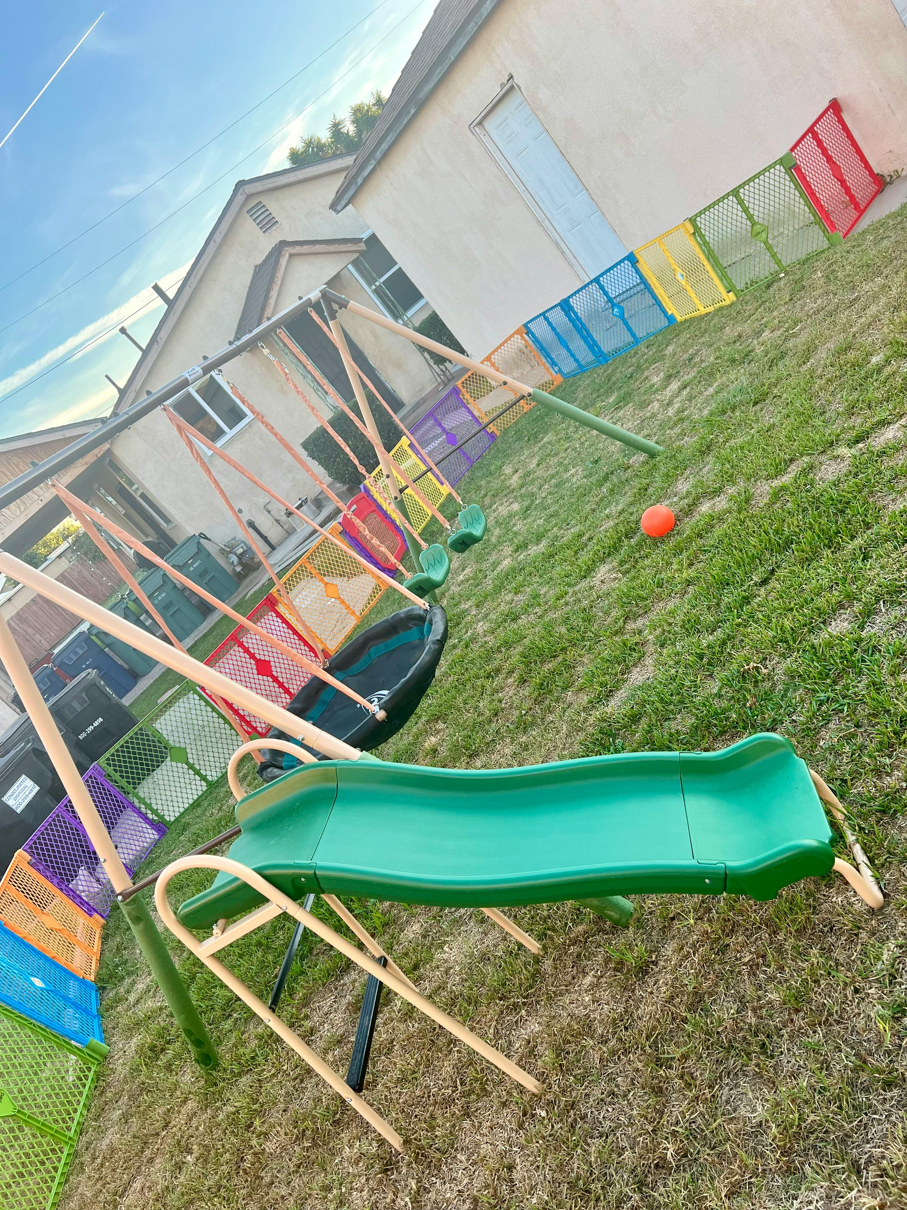Playground with swings, a slide, and a trampoline in a grassy yard