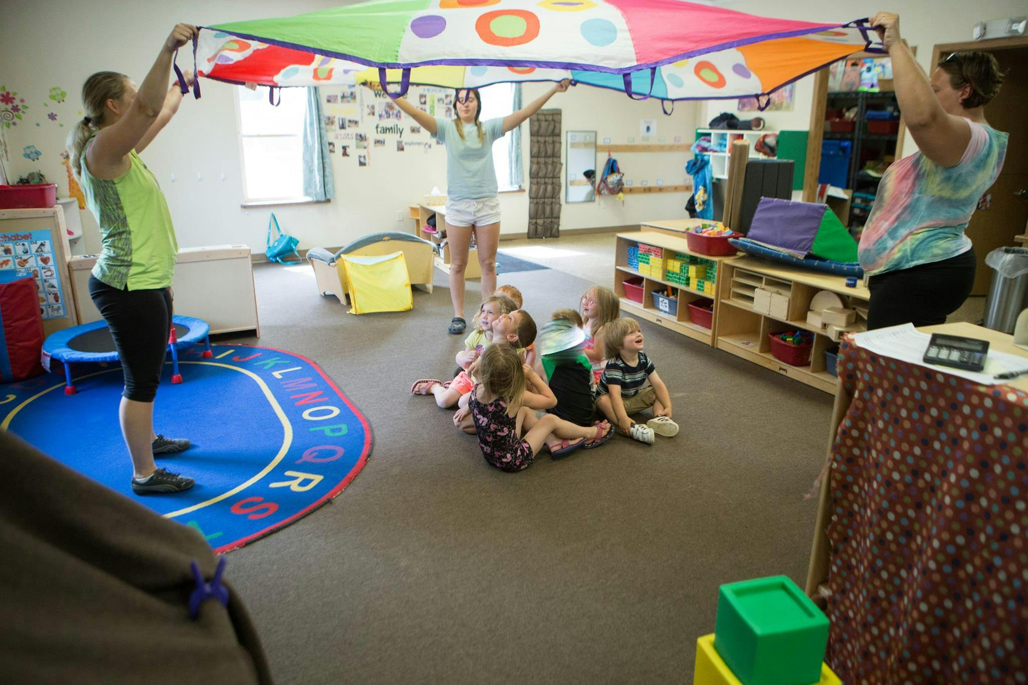 People and children playing with a colorful parachute in a classroom