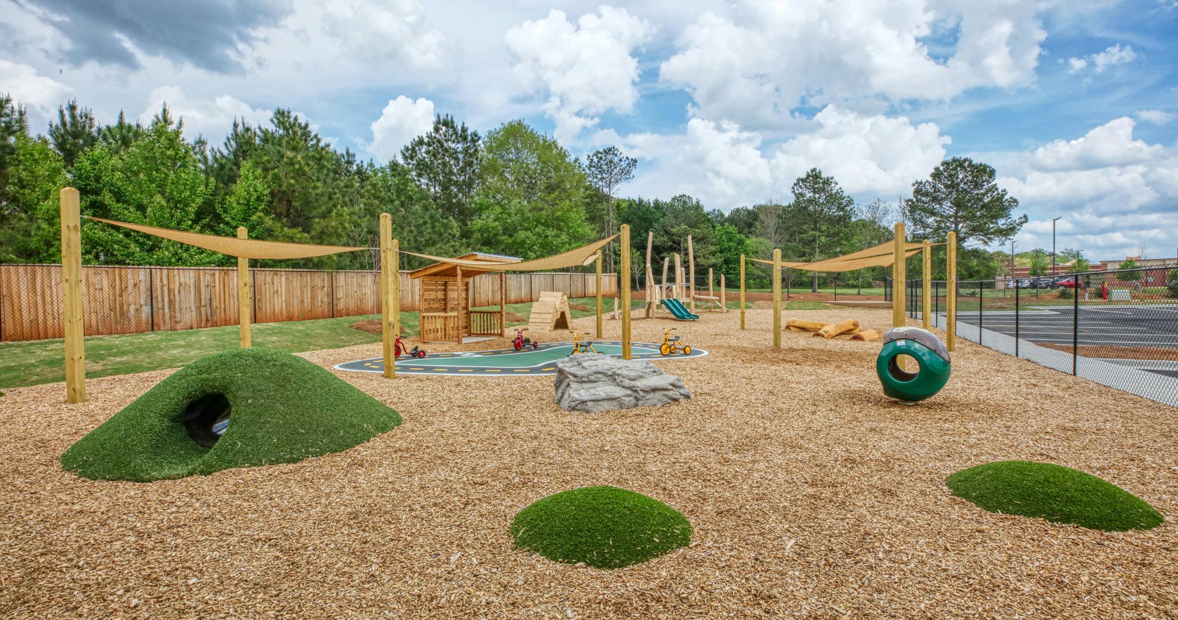 Outdoor playground with wood chips, shade sails, and various play structures