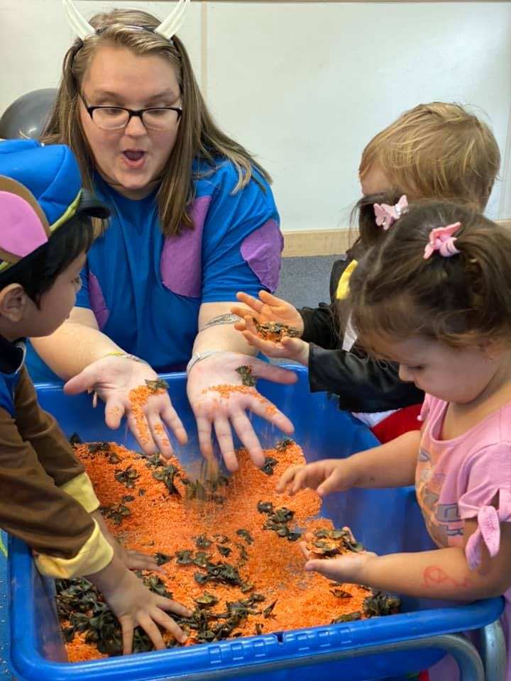 Adult and children playing with orange rice and dark objects in a blue bin