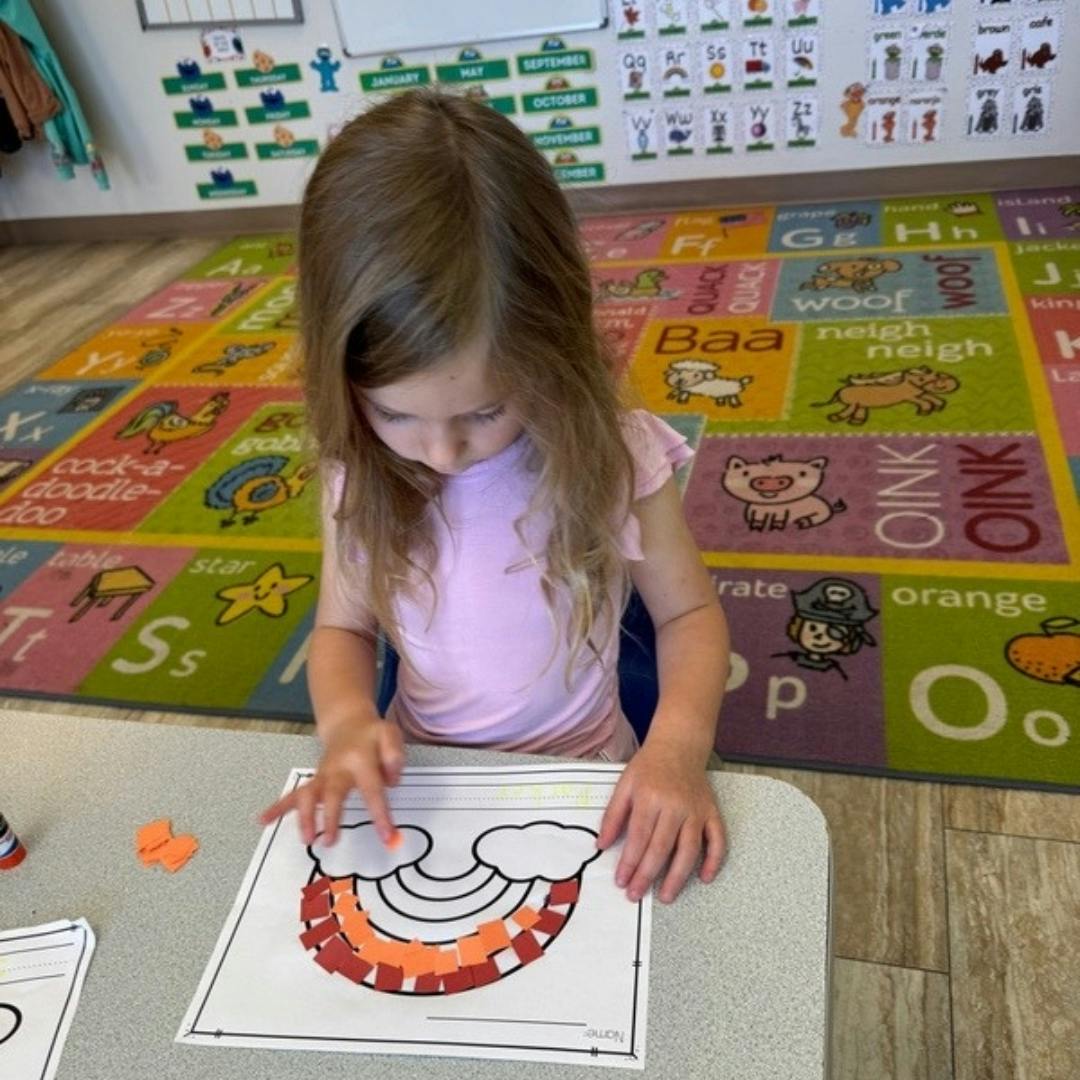 Child doing a craft with a rainbow outline