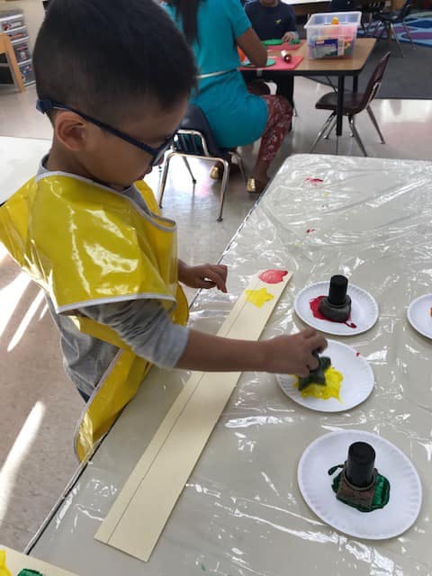 Child in yellow smock painting with a stamp