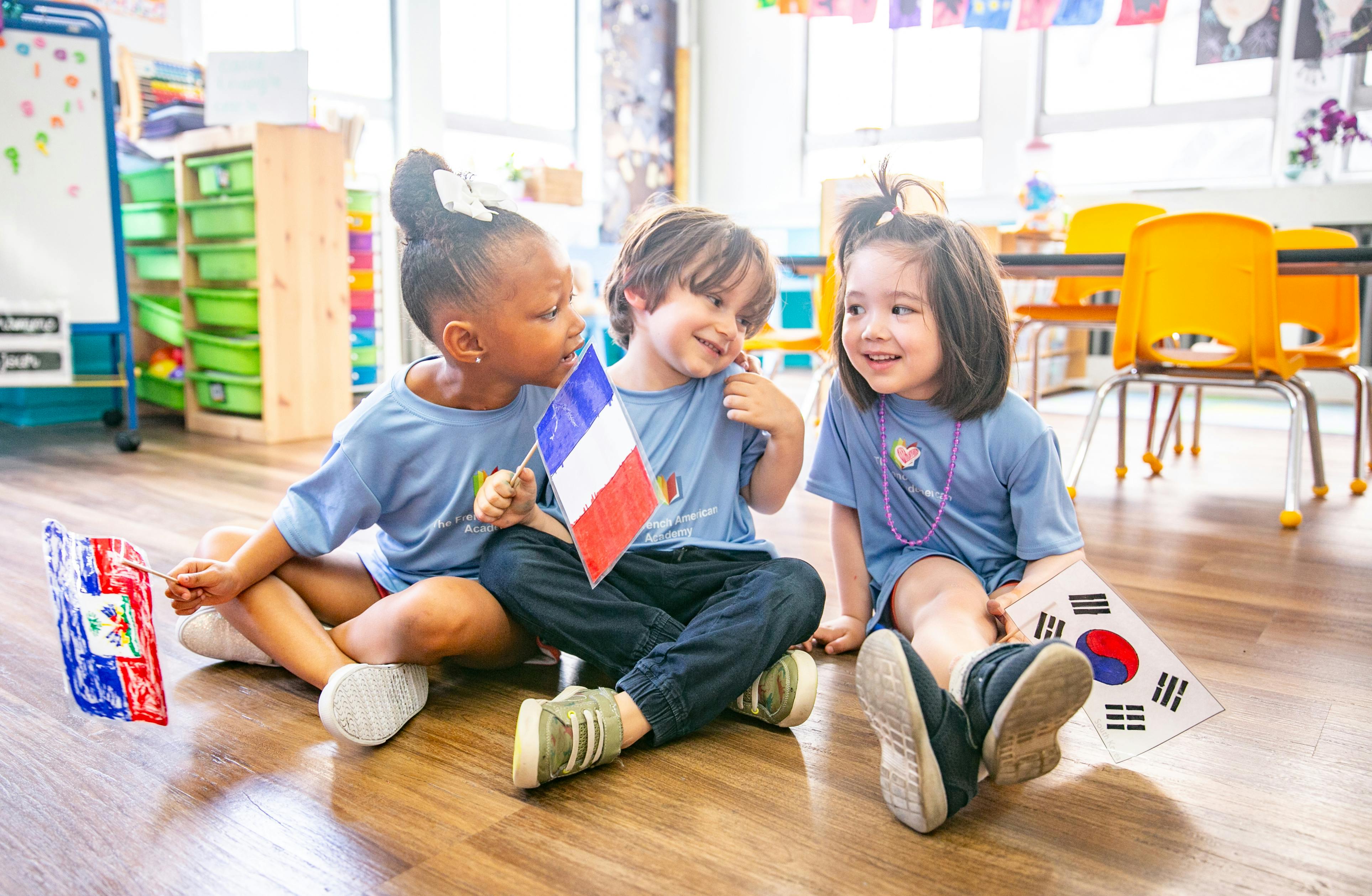 Three children sitting on the floor holding small flags