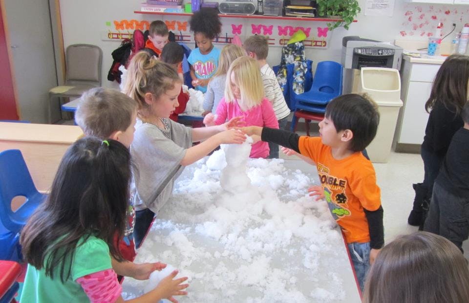 Children playing with white fluffy material in a classroom