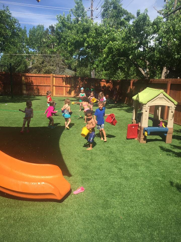 Children playing in a grassy backyard with a slide and playhouse