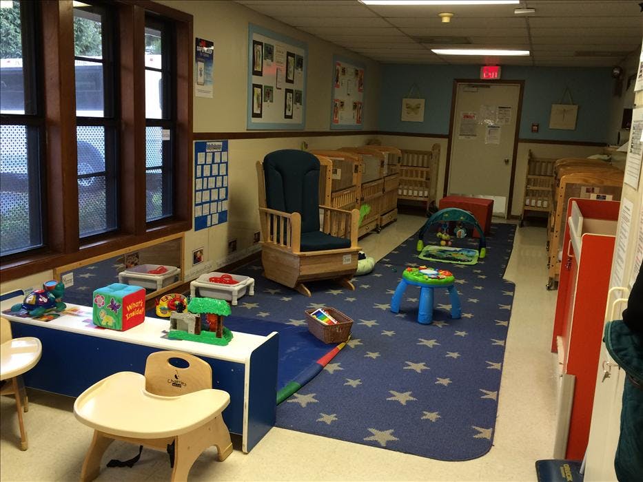 A playroom with cribs, a rocking chair, toys, and blue carpet with stars