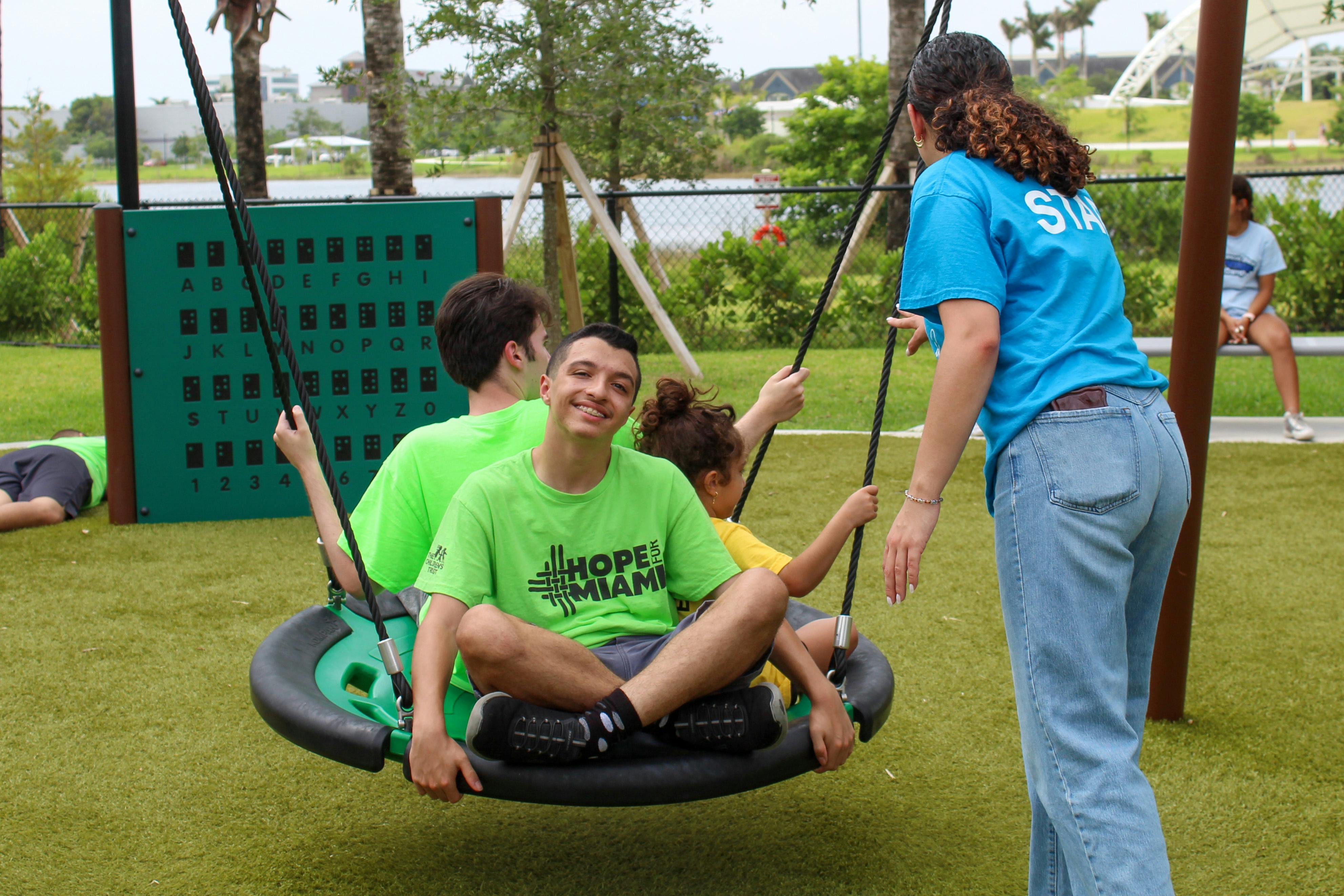 People on a playground saucer swing with a staff member standing nearby
