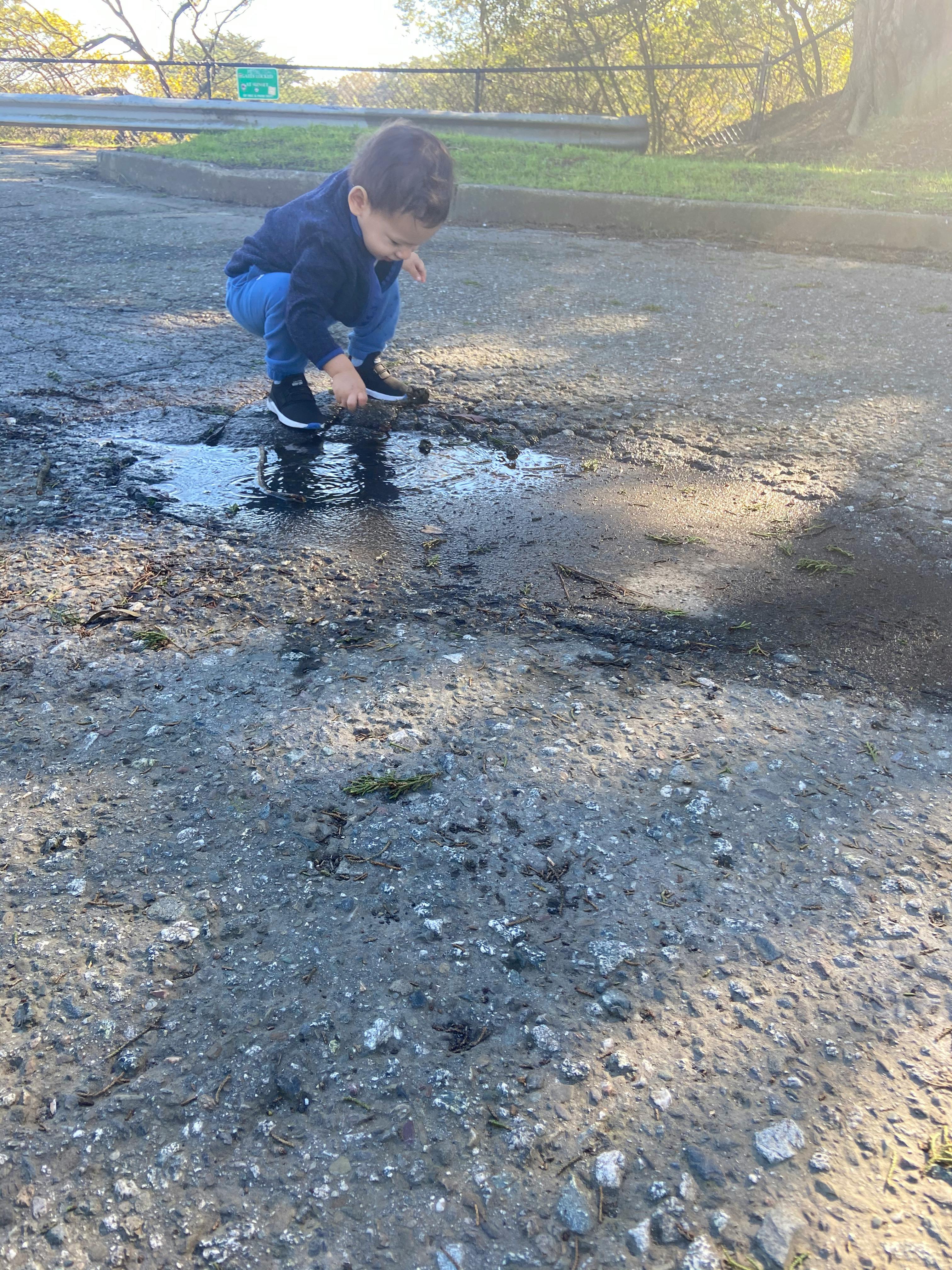 Child crouching and playing in a puddle on a paved surface