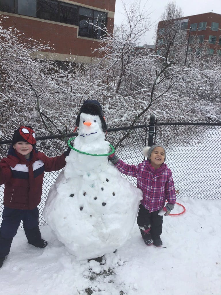 Two children standing next to a snowman
