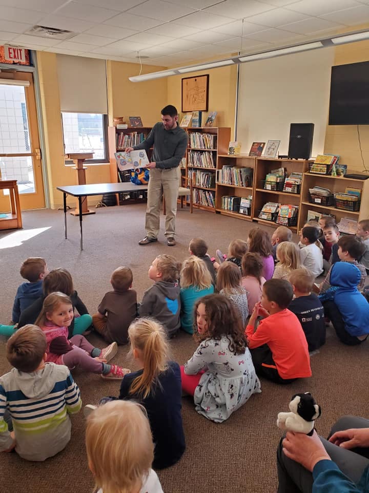 Adult holding a book and speaking to a group of children sitting on the floor