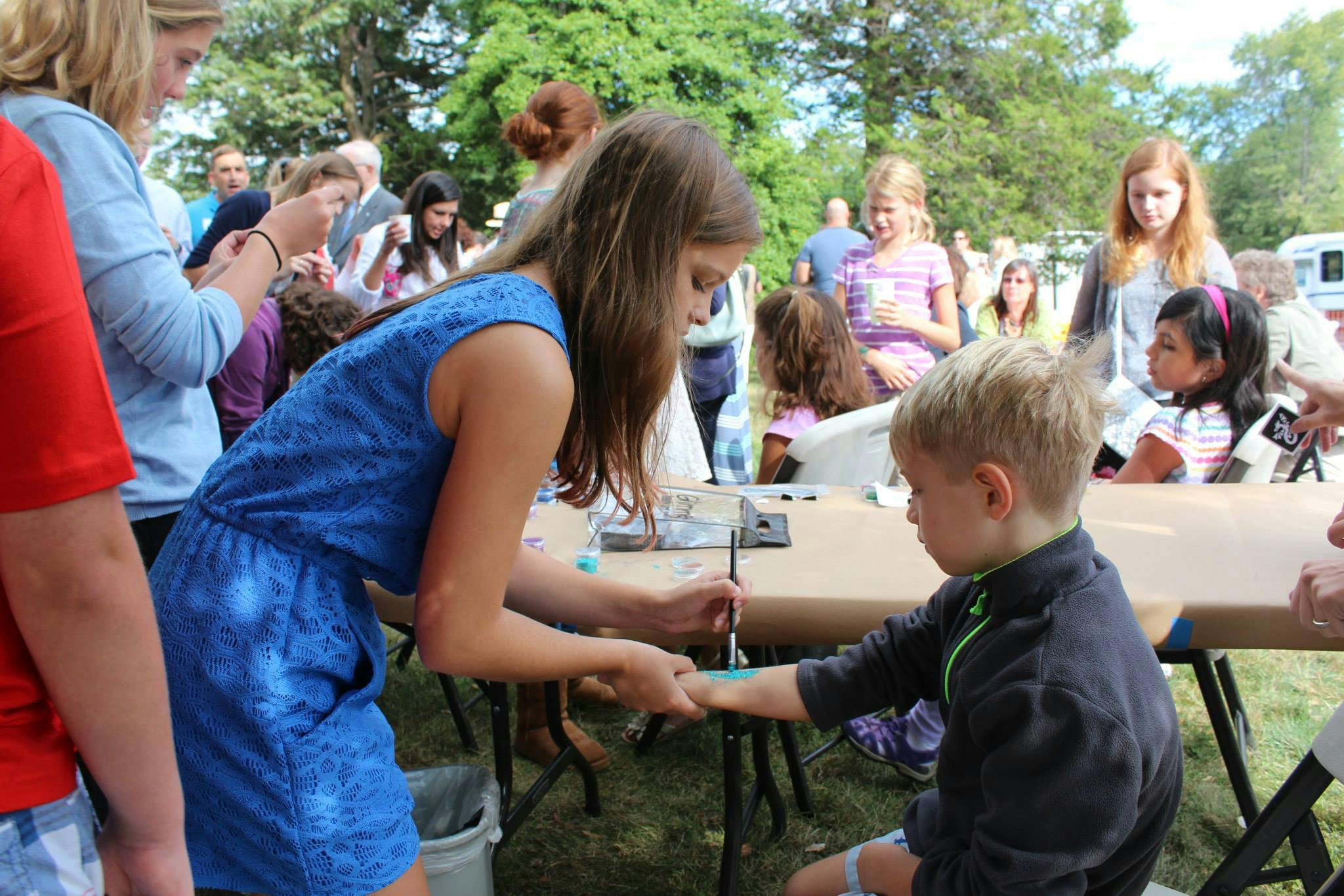 Person painting on a child's hand at a table outdoors