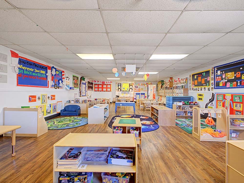 Empty preschool classroom with colorful decorations, rugs, and child-sized furniture
