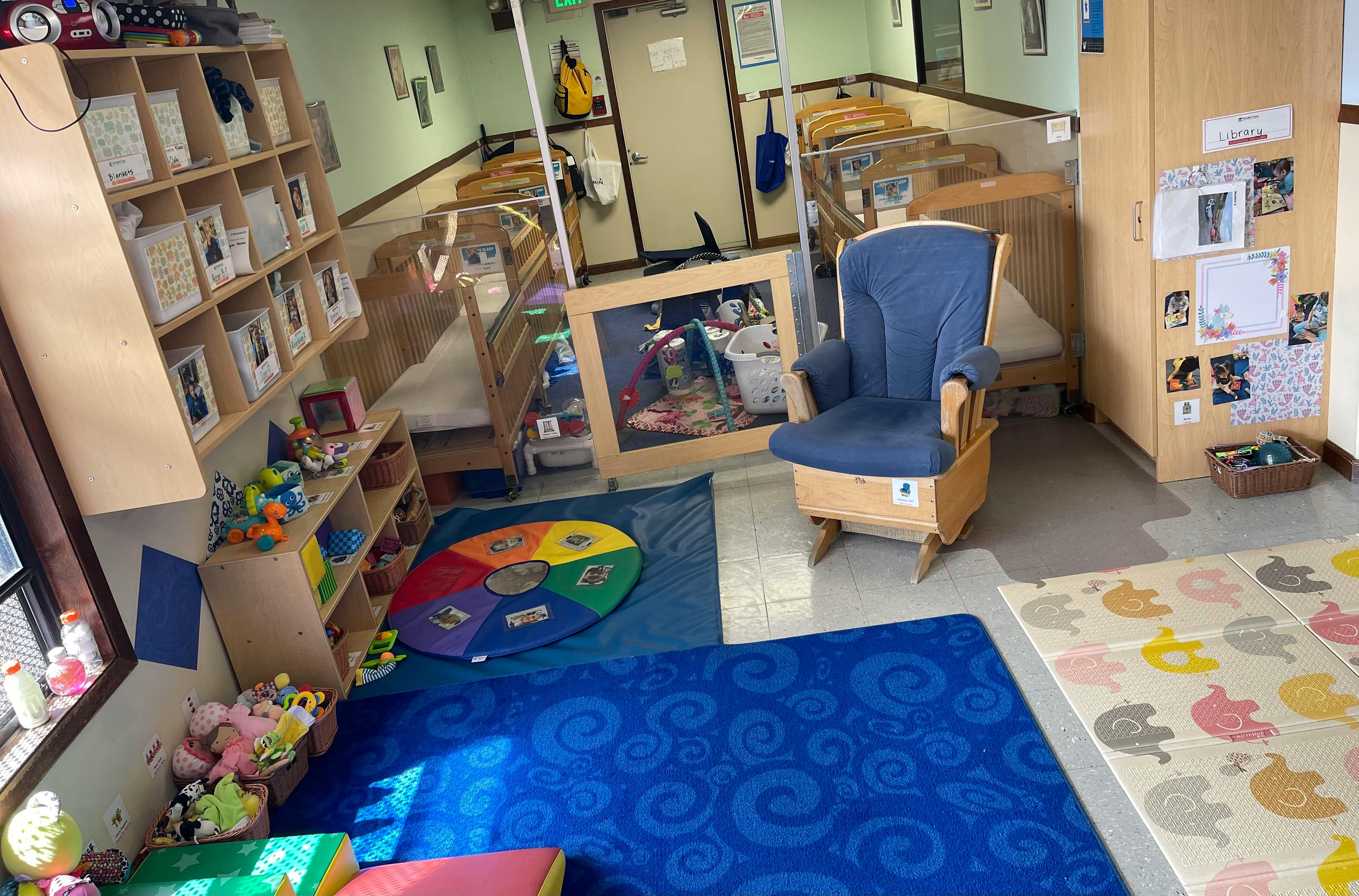 Classroom with cribs, a blue rocking chair, toy shelves, and play mats
