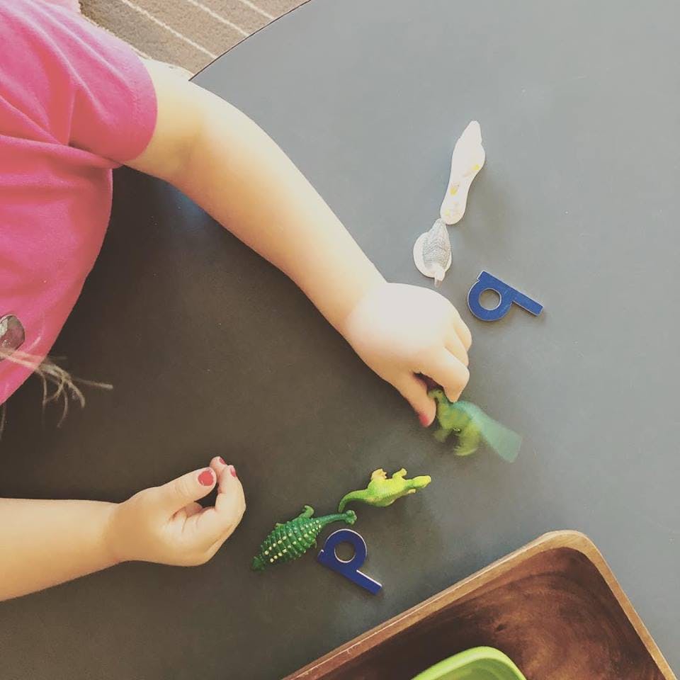 Child playing with small dinosaur toys and letter shapes on a table