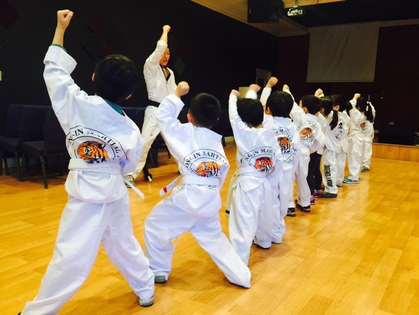 Children in white uniforms practicing martial arts with an instructor