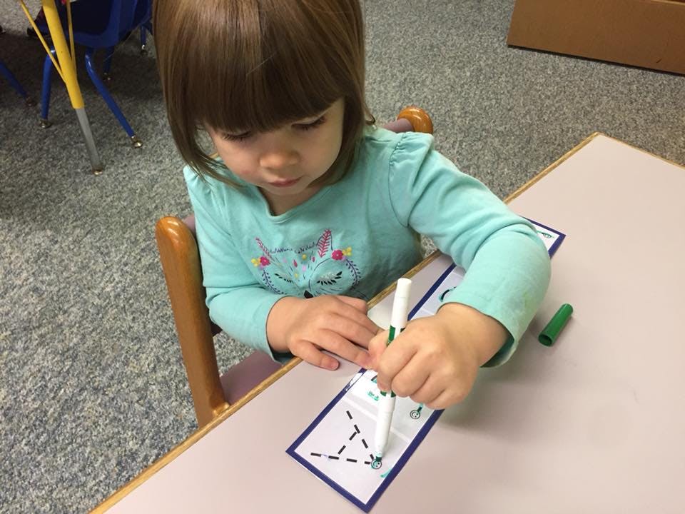 Child tracing a shape on paper with a green marker