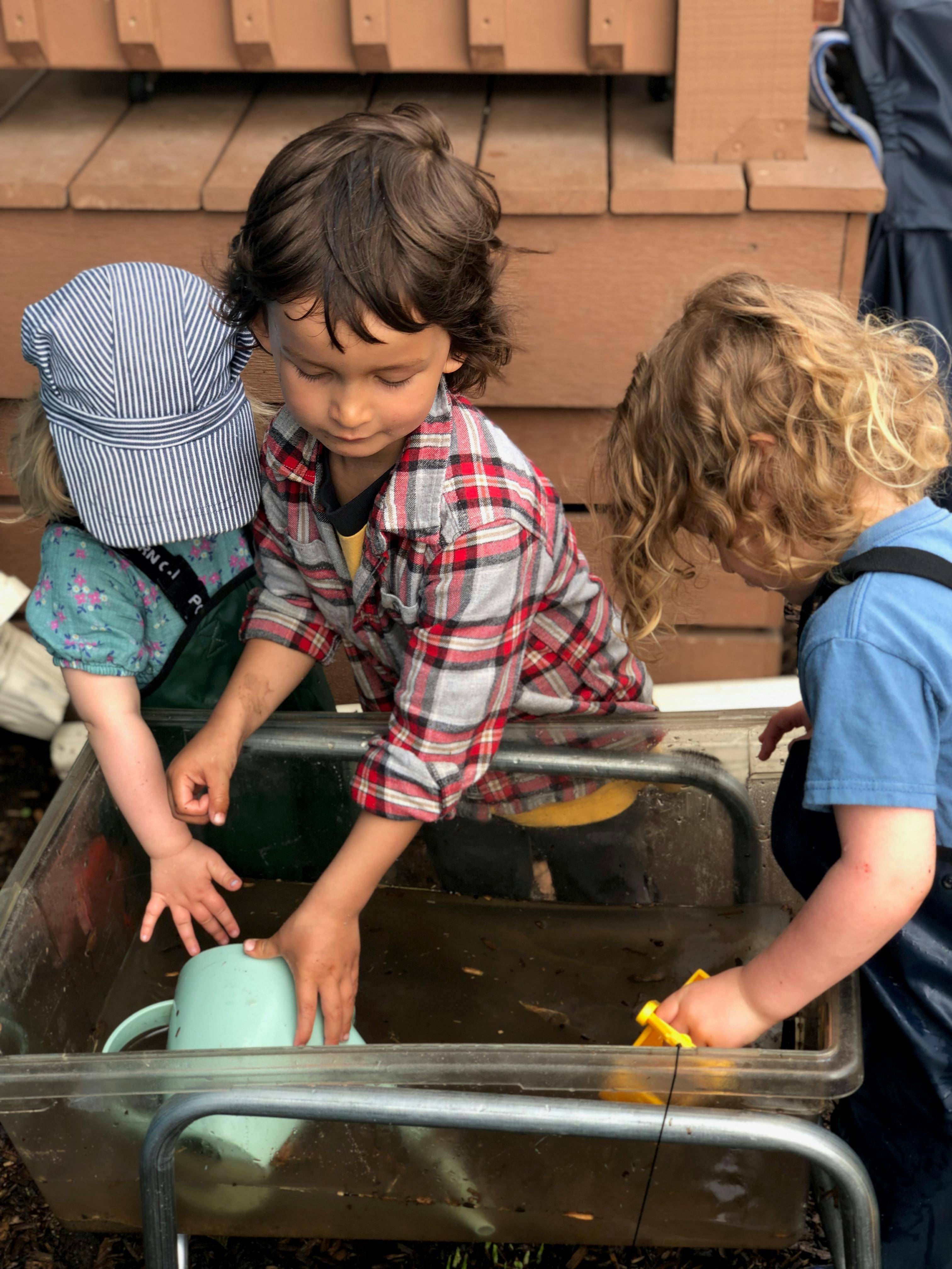 Three children playing with water in a trough