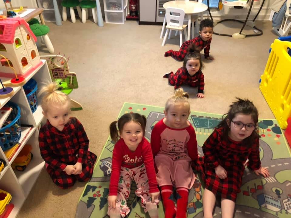 Multiple children in a playroom, some sitting on a rug, others crawling