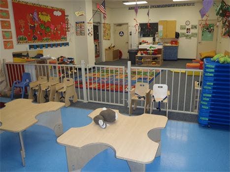 Classroom with small tables and chairs, playpen, and colorful rug