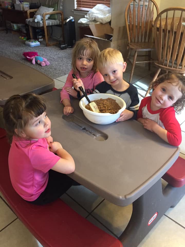 Four children sitting at a small table with a bowl of food