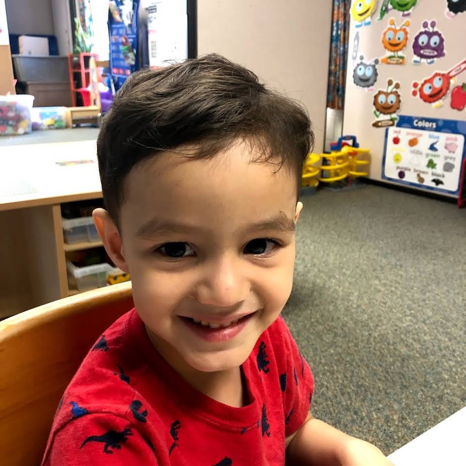 Child in a red shirt smiling in a classroom