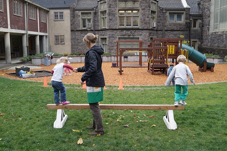 Person helping a child on a balance beam, another child on the beam