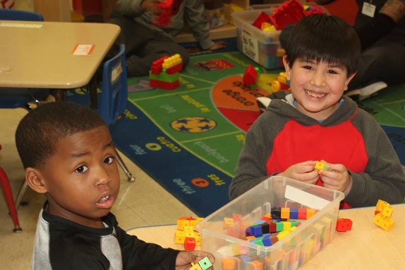 Two children playing with colorful building blocks in a classroom