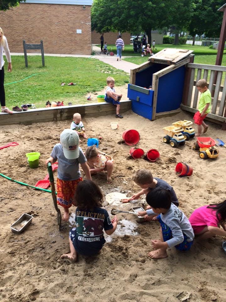 Children playing in a large sandbox with toys