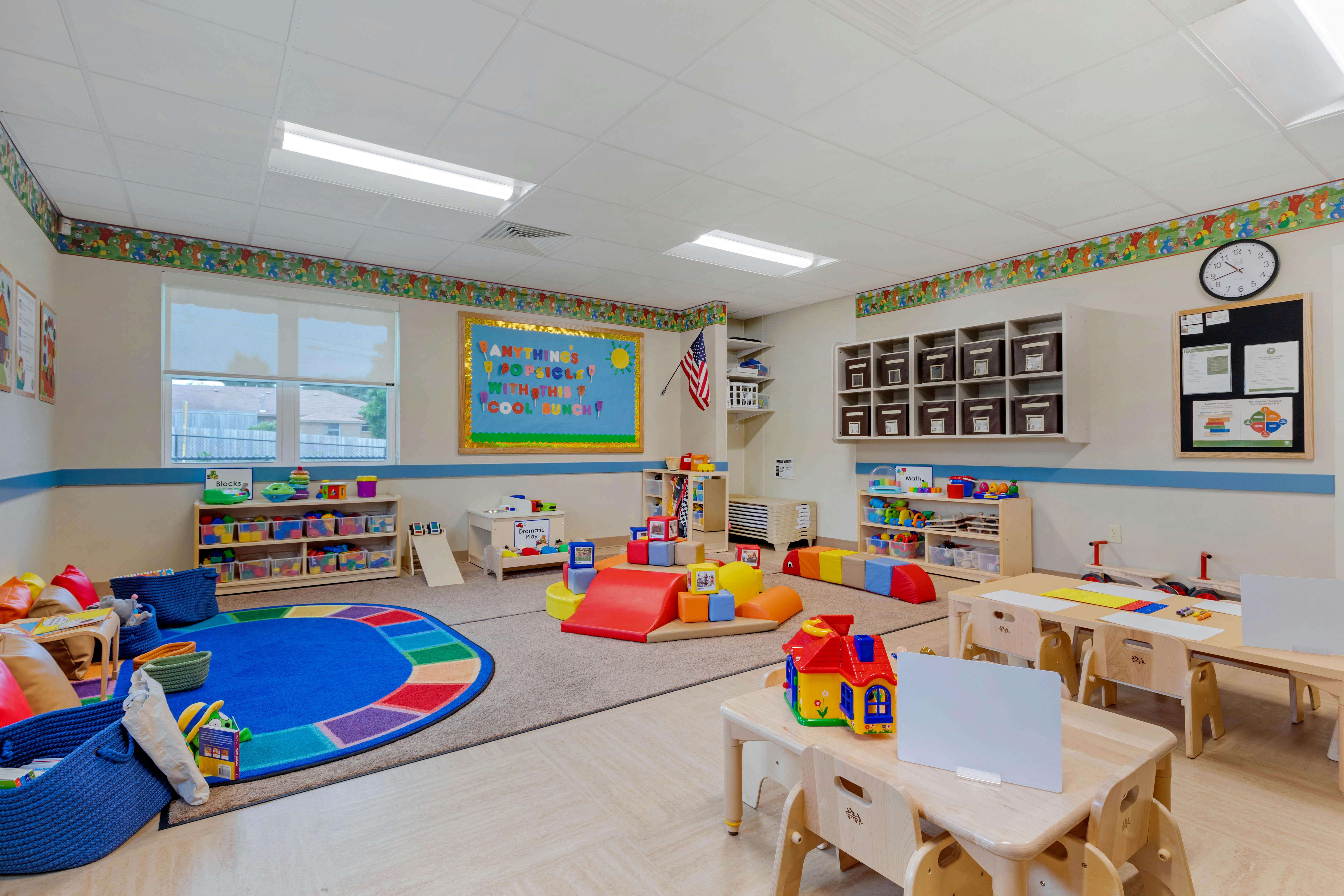 Colorful playroom with small tables and chairs, shelves of toys, and a blue rug
