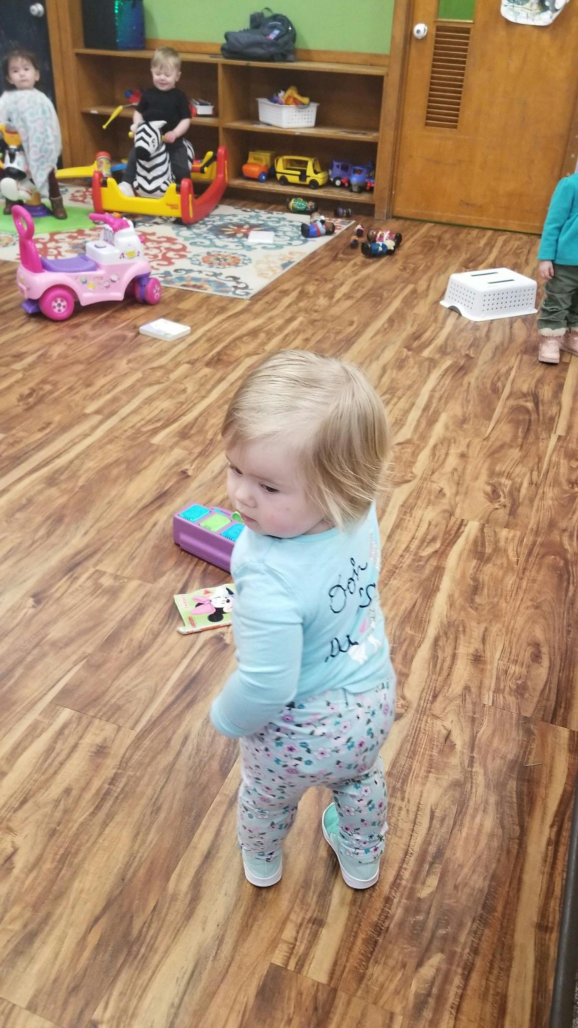 Child standing on a wooden floor in a room with toys