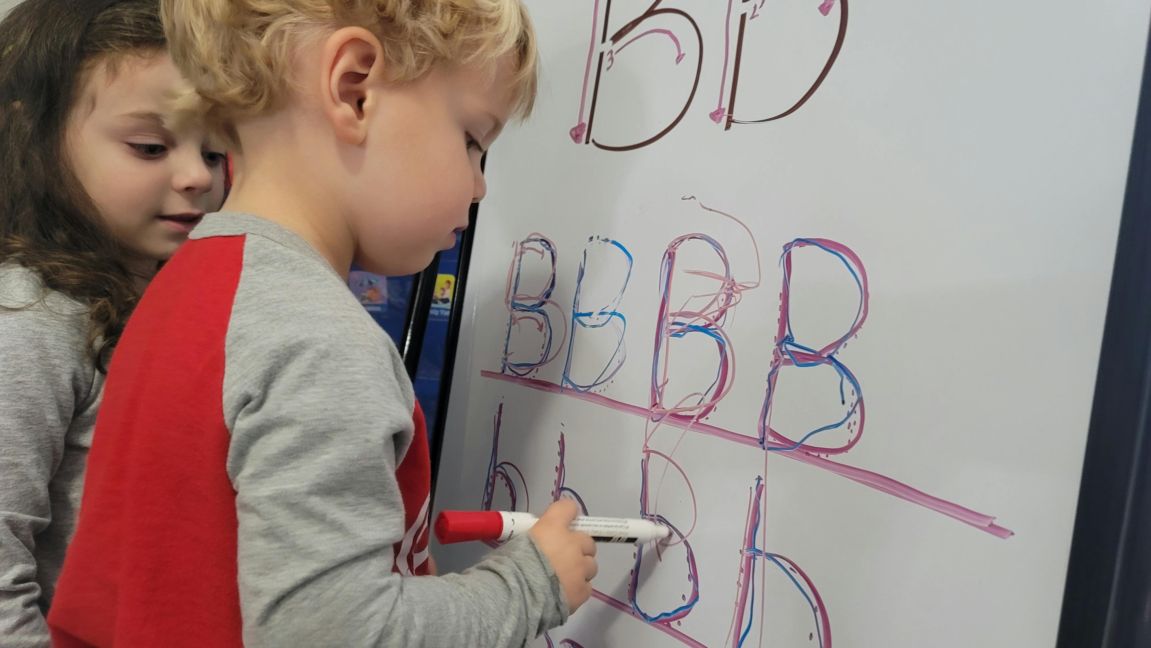 Child writing letters on a whiteboard with a marker