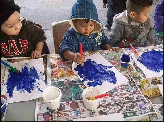Three children painting with blue paint on paper