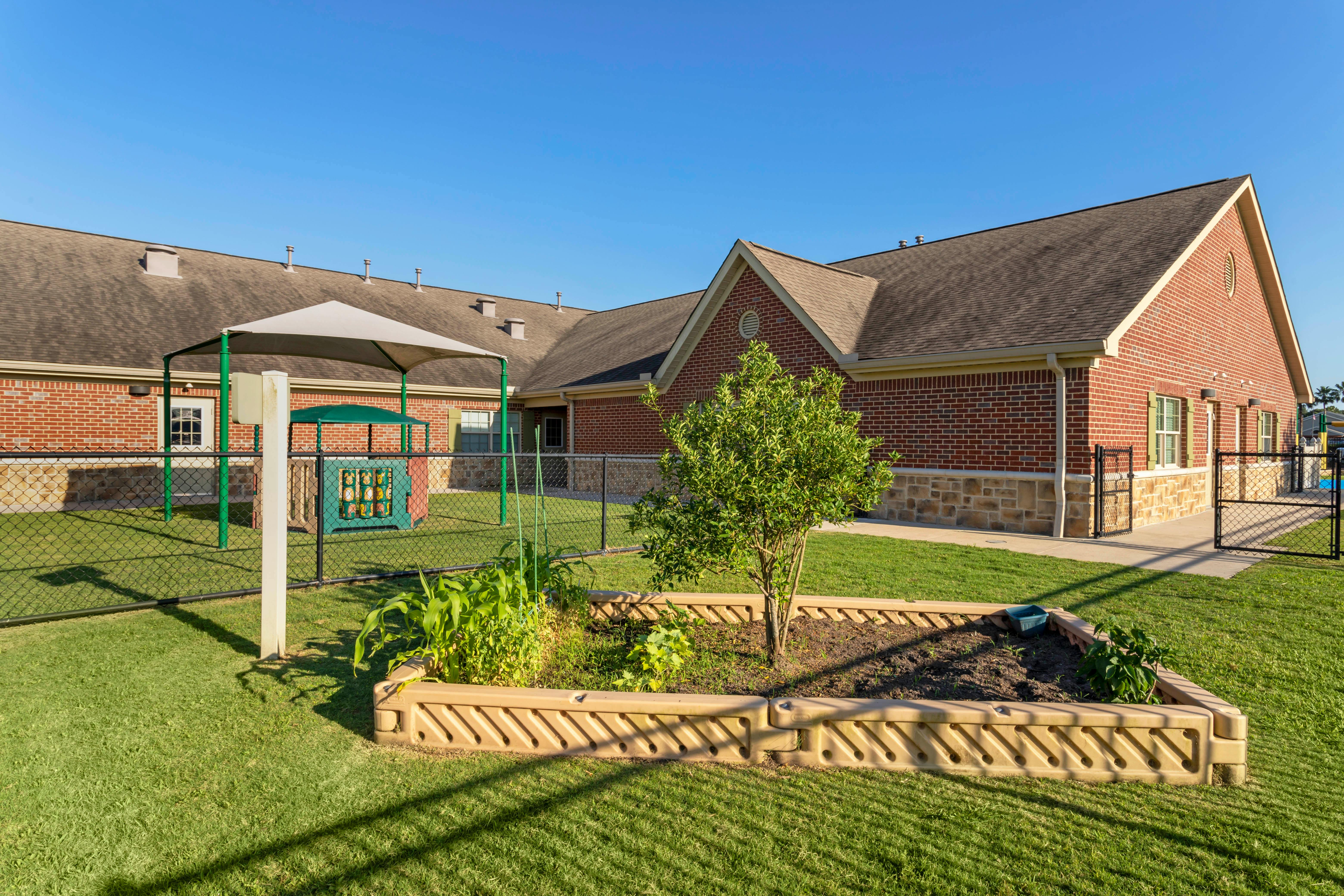 A fenced playground area with a small garden in the foreground