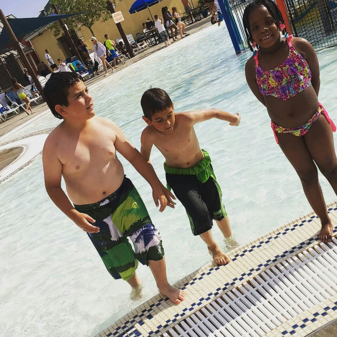 Three children standing in shallow water at a pool