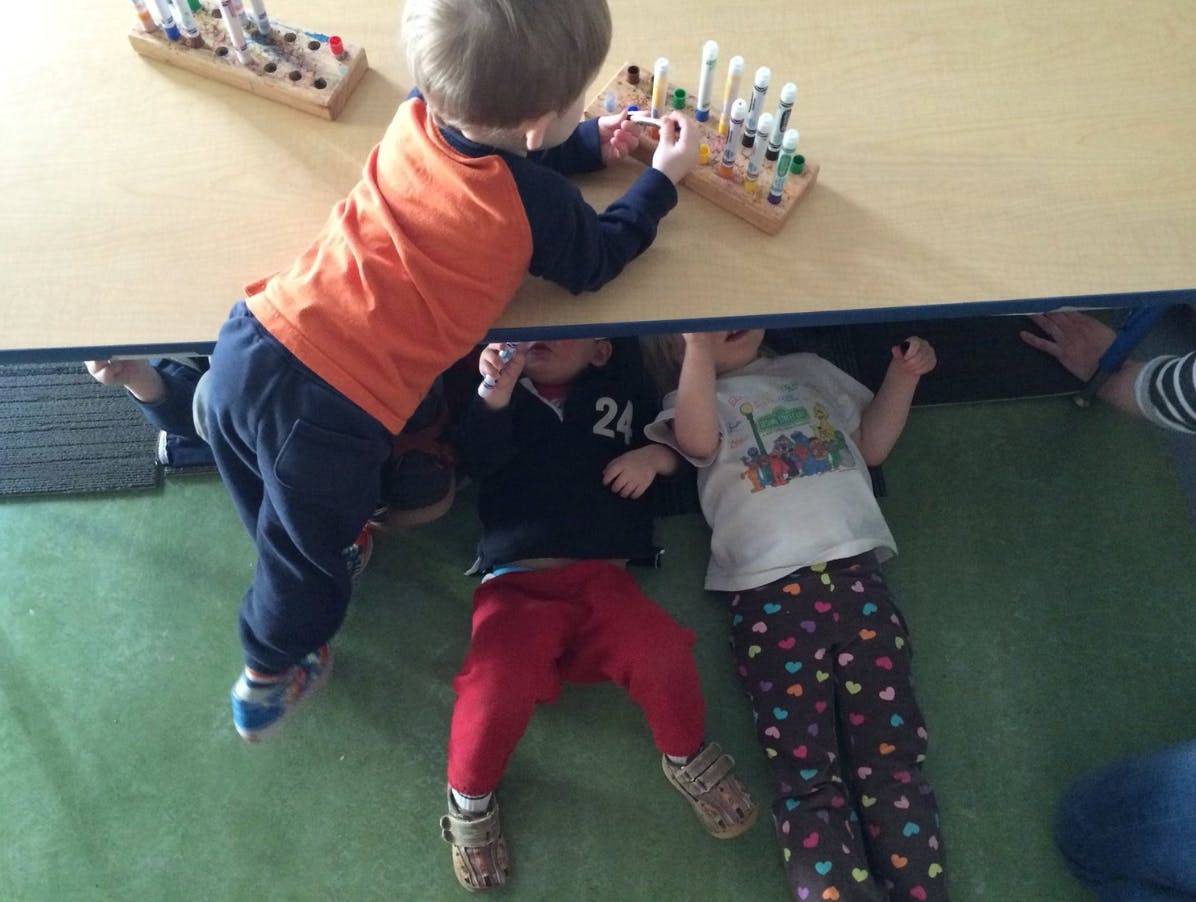 Three children playing around a table, one on top and two underneath